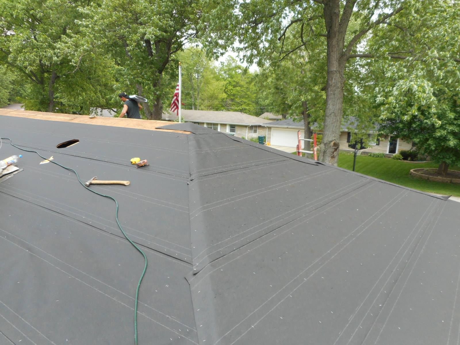 Roofing work in progress; black underlayment covers a multi-faceted roof with a worker in the background.