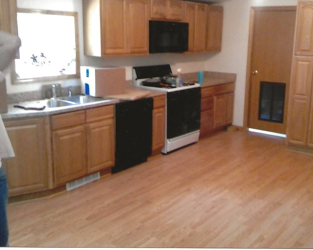 Kitchen with light wood cabinets, black appliances, and a wood floor.