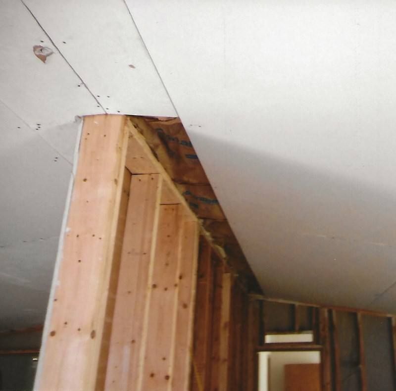 Interior view of a partially constructed wall with exposed wooden framing and drywall on the ceiling.