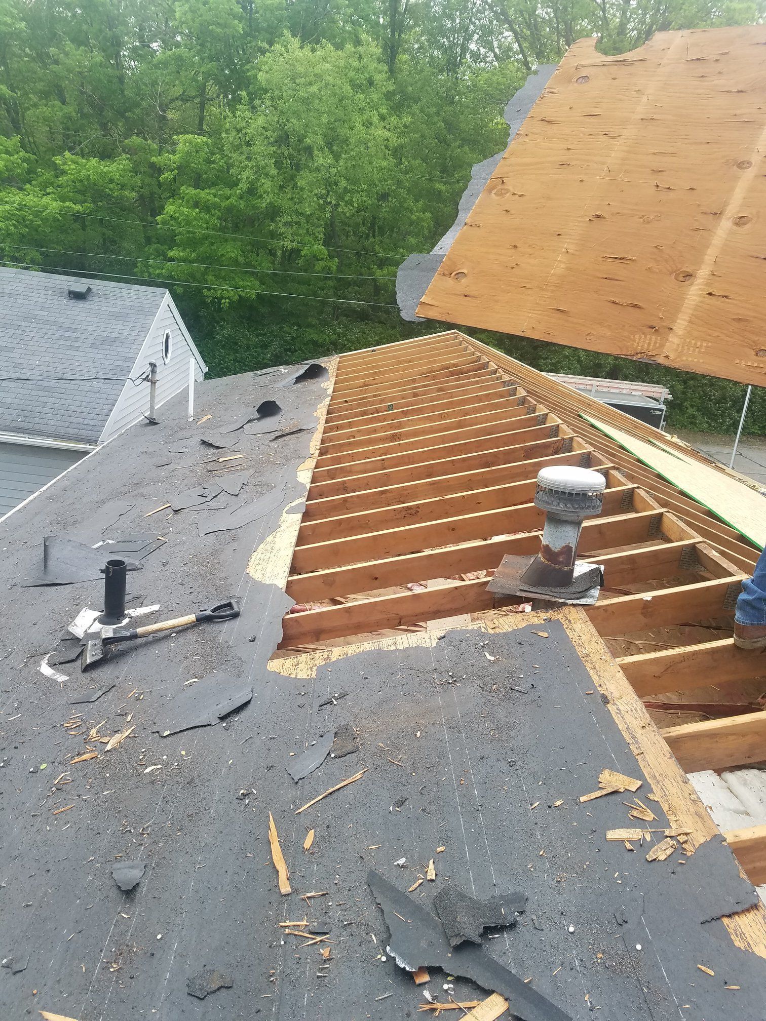 Roof in mid-repair; old shingles removed, exposing wood frame and underlayment.
