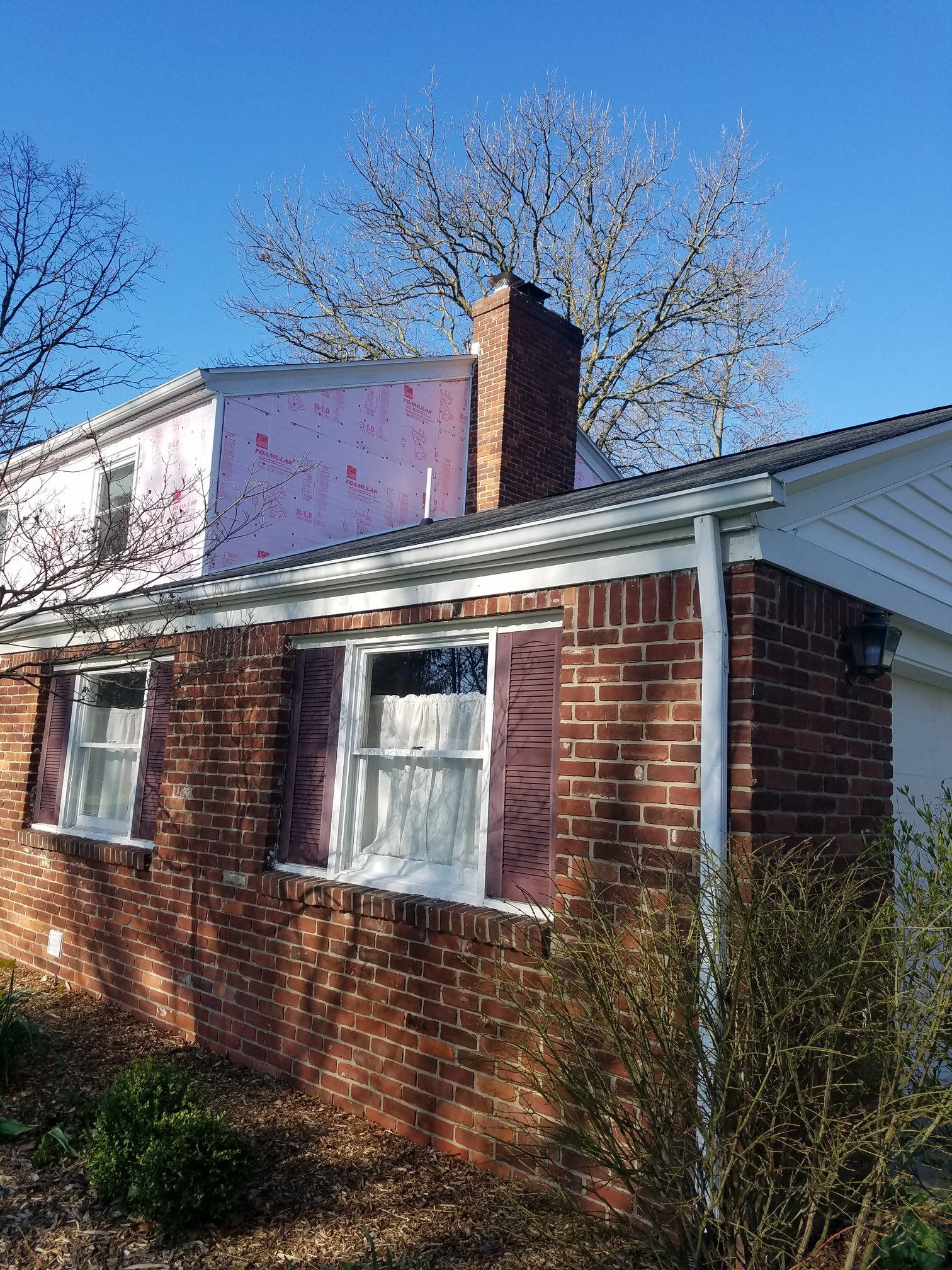 Red brick house with a chimney, windows, and a pink-painted addition under a blue sky.