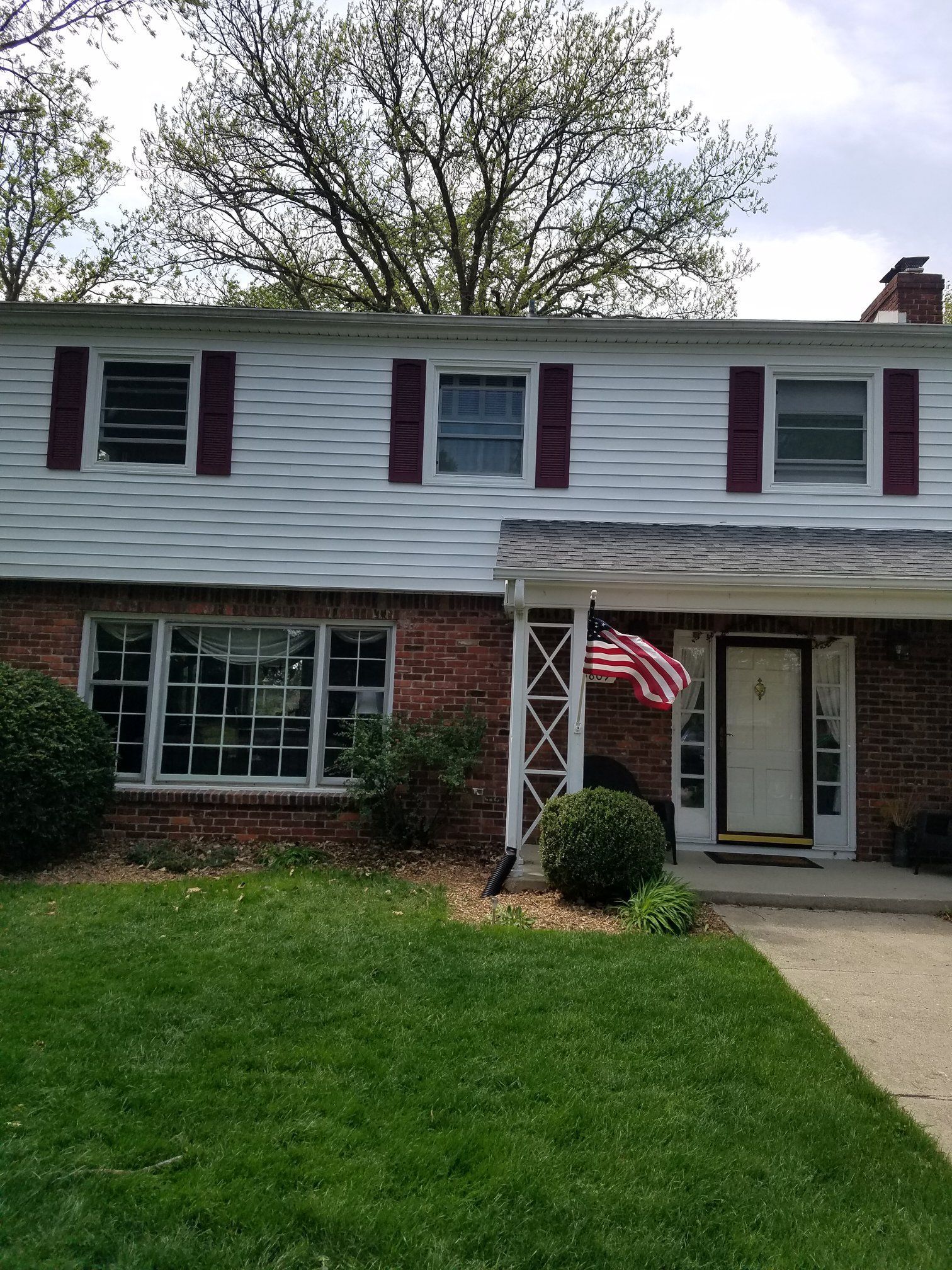 Two-story brick house with white siding, maroon shutters, and an American flag.