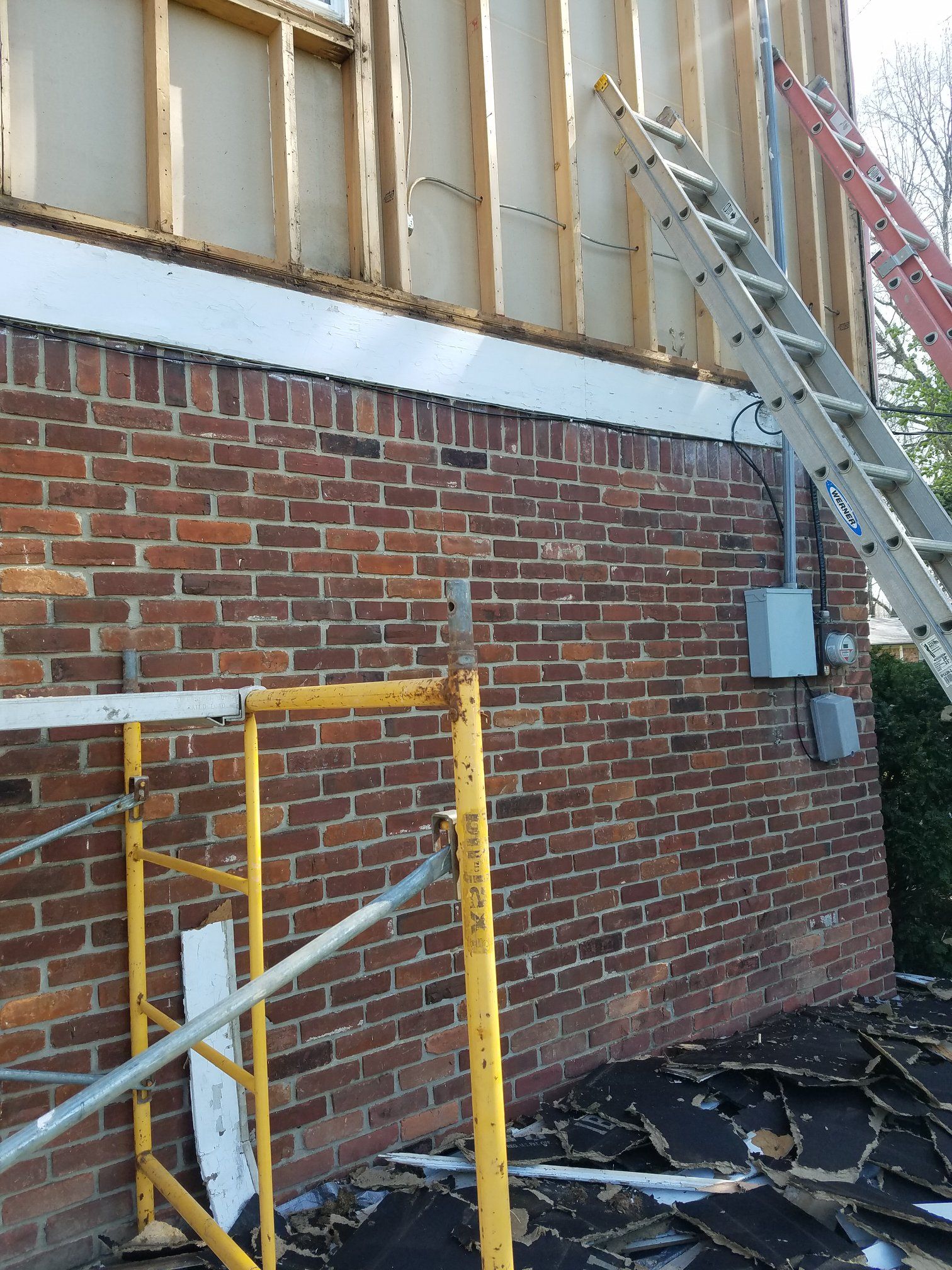 Brick building exterior with exposed wooden framing above. Ladders and scaffolding are present.