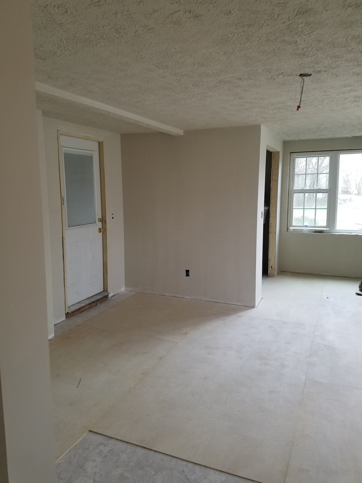 Interior room under construction with white walls, a doorway, and a window.