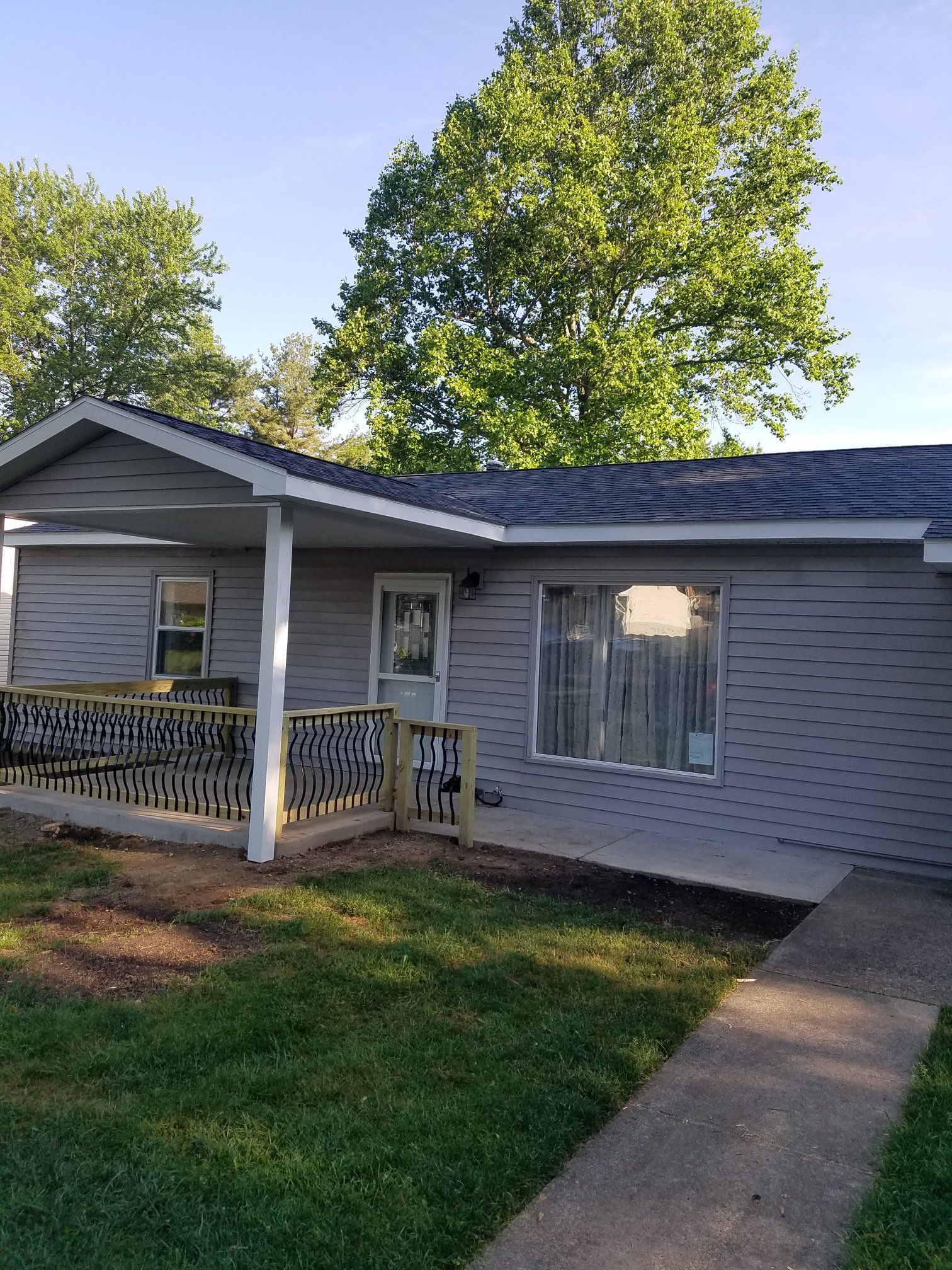Gray house with a porch and new wooden deck, in a grassy yard.
