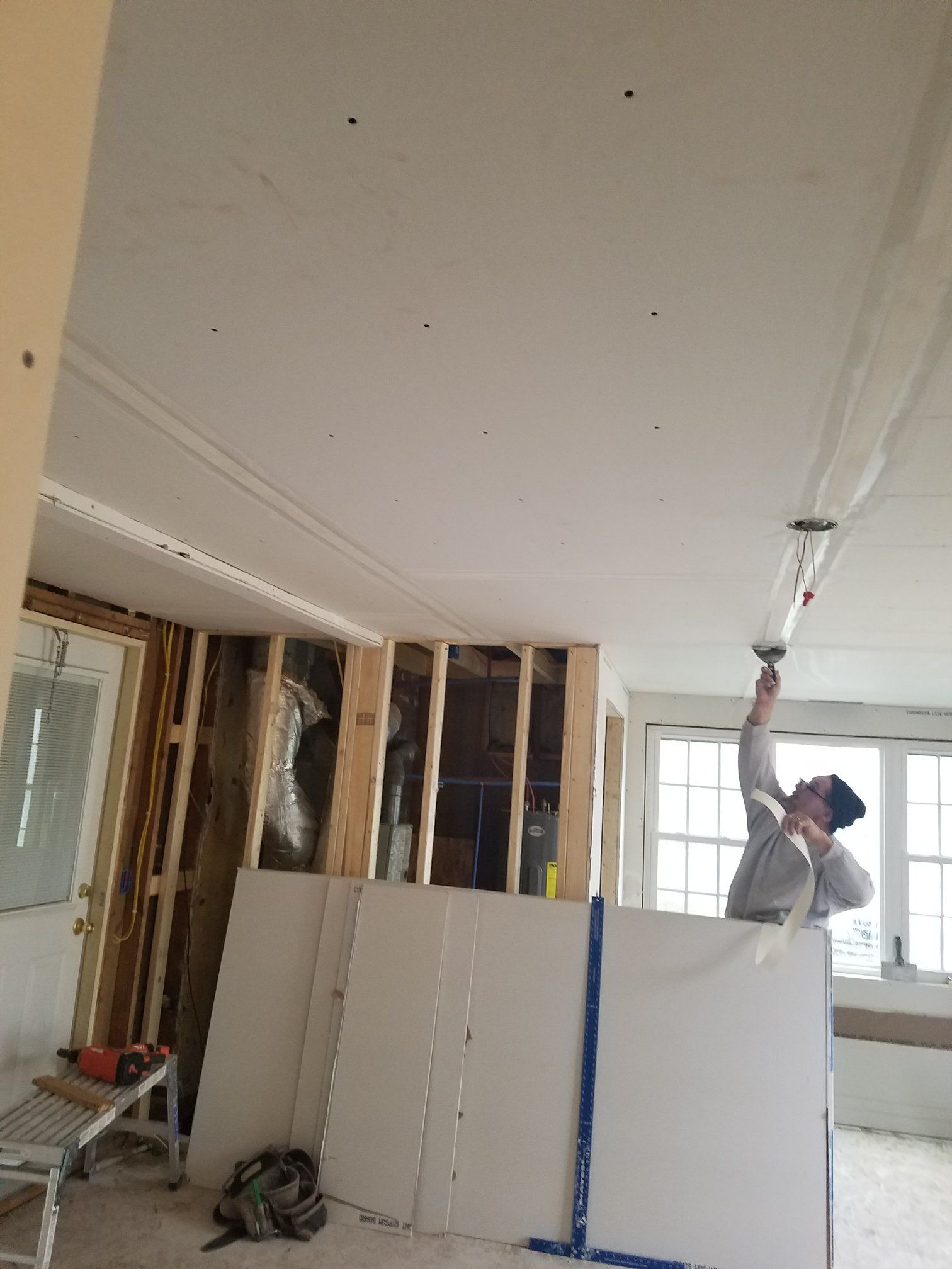 Person taping drywall ceiling with a long-handled tool in a room under construction.