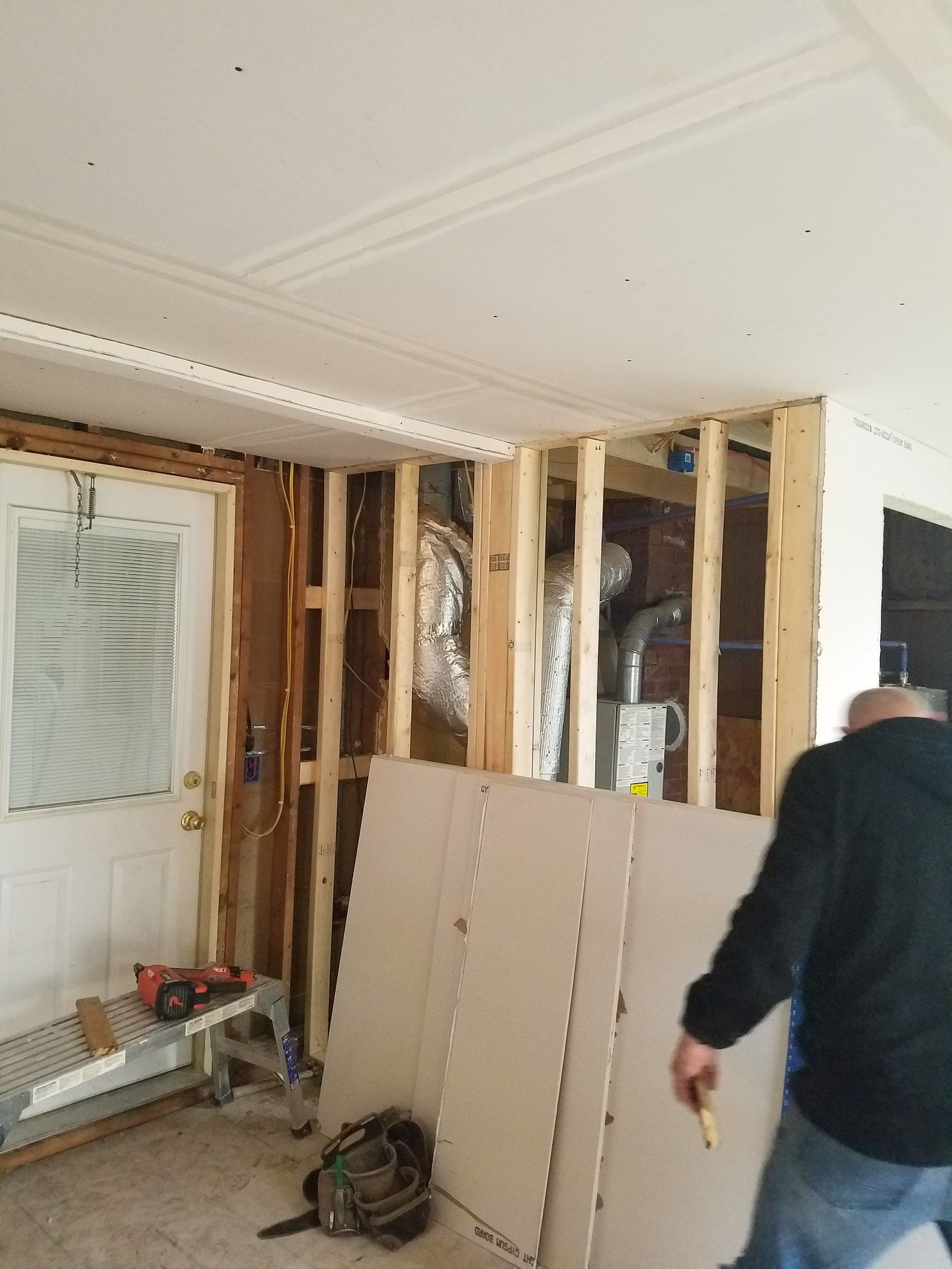Interior construction site with exposed studs, drywall, HVAC equipment, and person working.