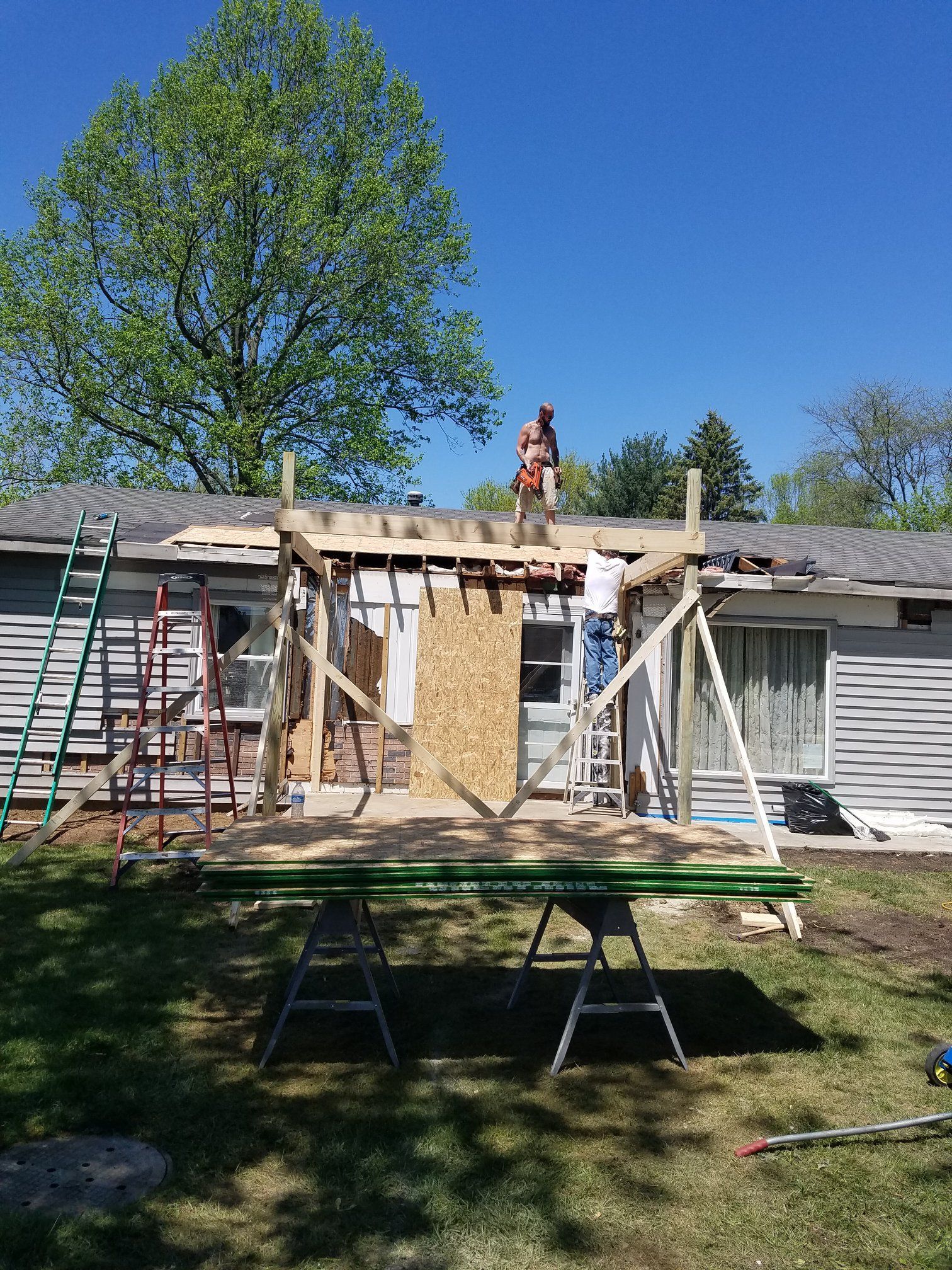 Construction workers building a wooden structure on a house roof on a sunny day.