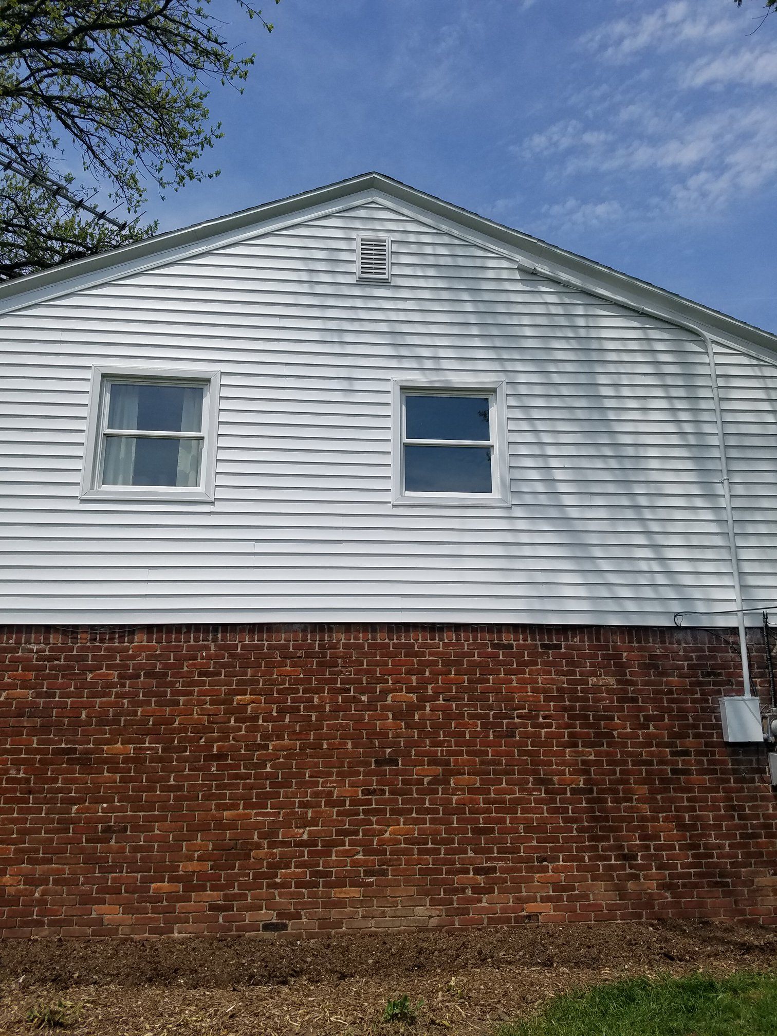White siding above a brick foundation; two windows and a vent on the side of a house.
