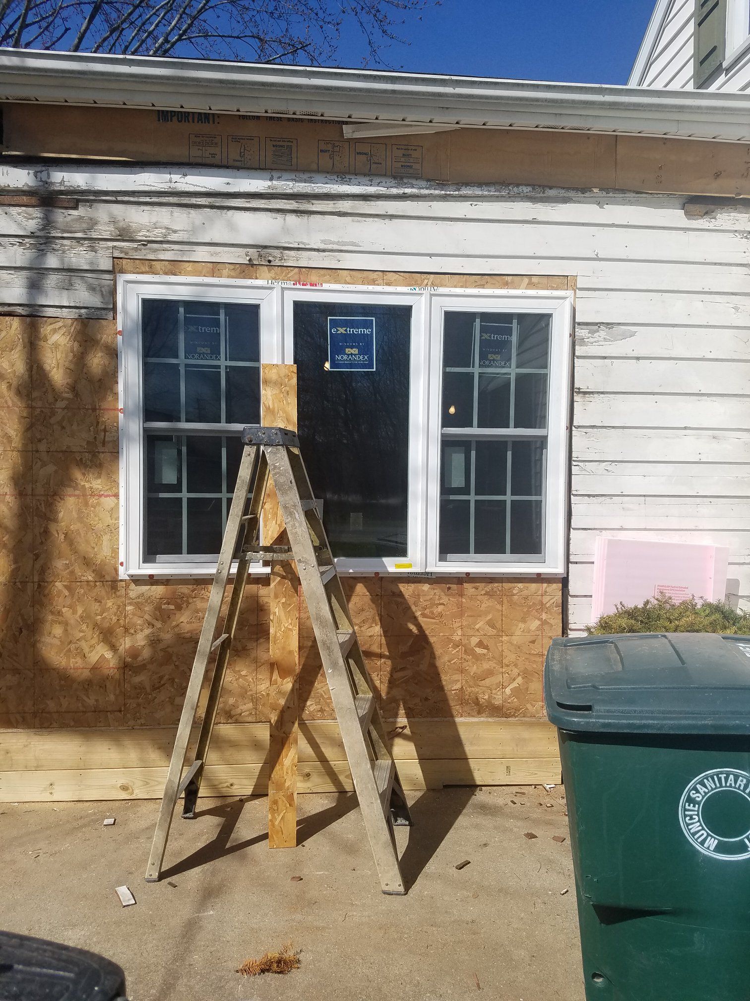 Exterior view of a building with a newly installed triple-pane window; a wooden ladder stands in front.