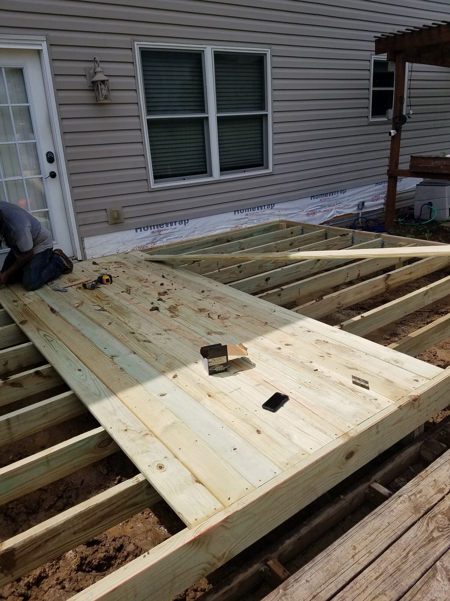 Deck being built; wooden planks laid over joists, near a house with windows.