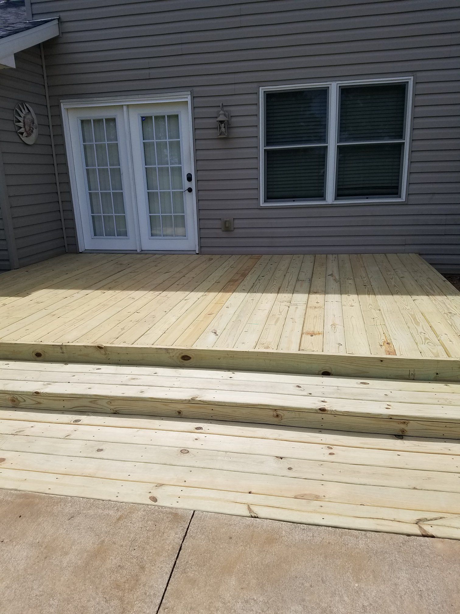 Wooden deck with steps leading to a glass door and a window on a gray house exterior.