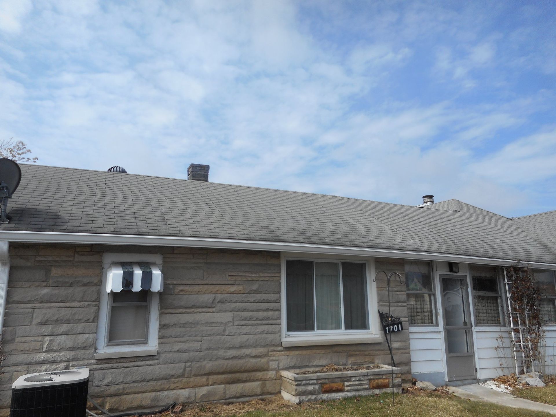Gray brick house with gray roof under a cloudy blue sky.