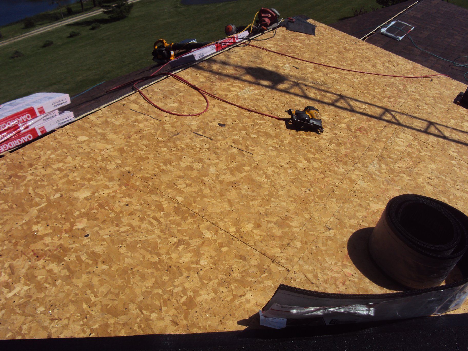 Roof under construction with plywood sheathing, tools, and a roll of roofing material.