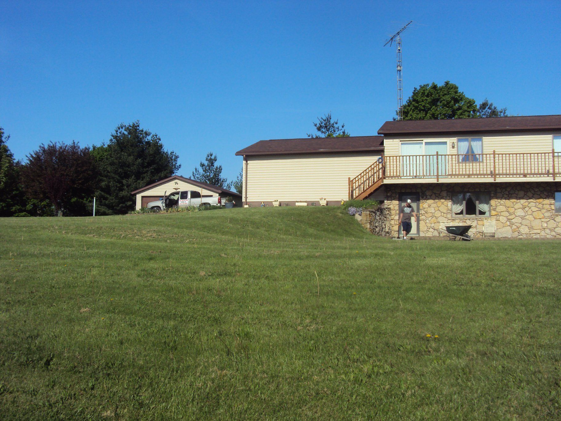 House with a garage on a grassy hill under a blue sky; an outdoor deck is visible.