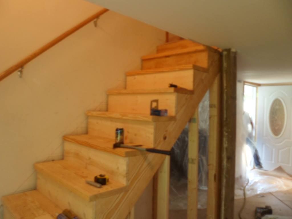Wooden staircase under construction, featuring steps and a handrail. Tools are visible on the steps.