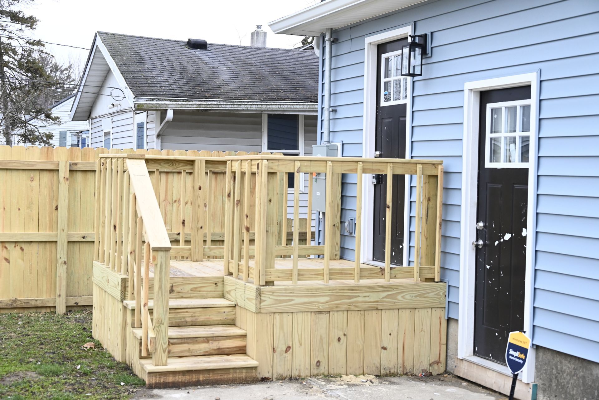 Wooden deck with stairs next to a blue house with two dark doors and a white window.