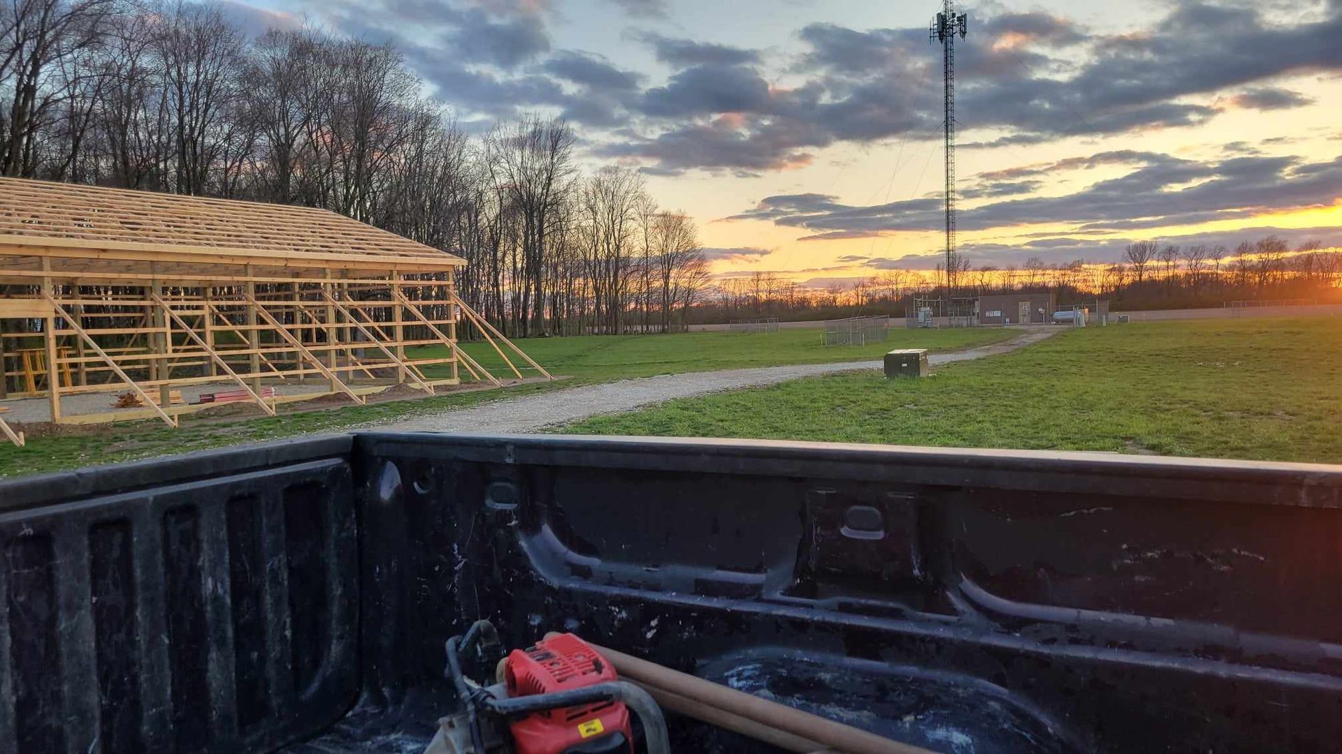 Construction site at sunset with a wooden frame, trees, a utility pole, and tools in a truck bed.