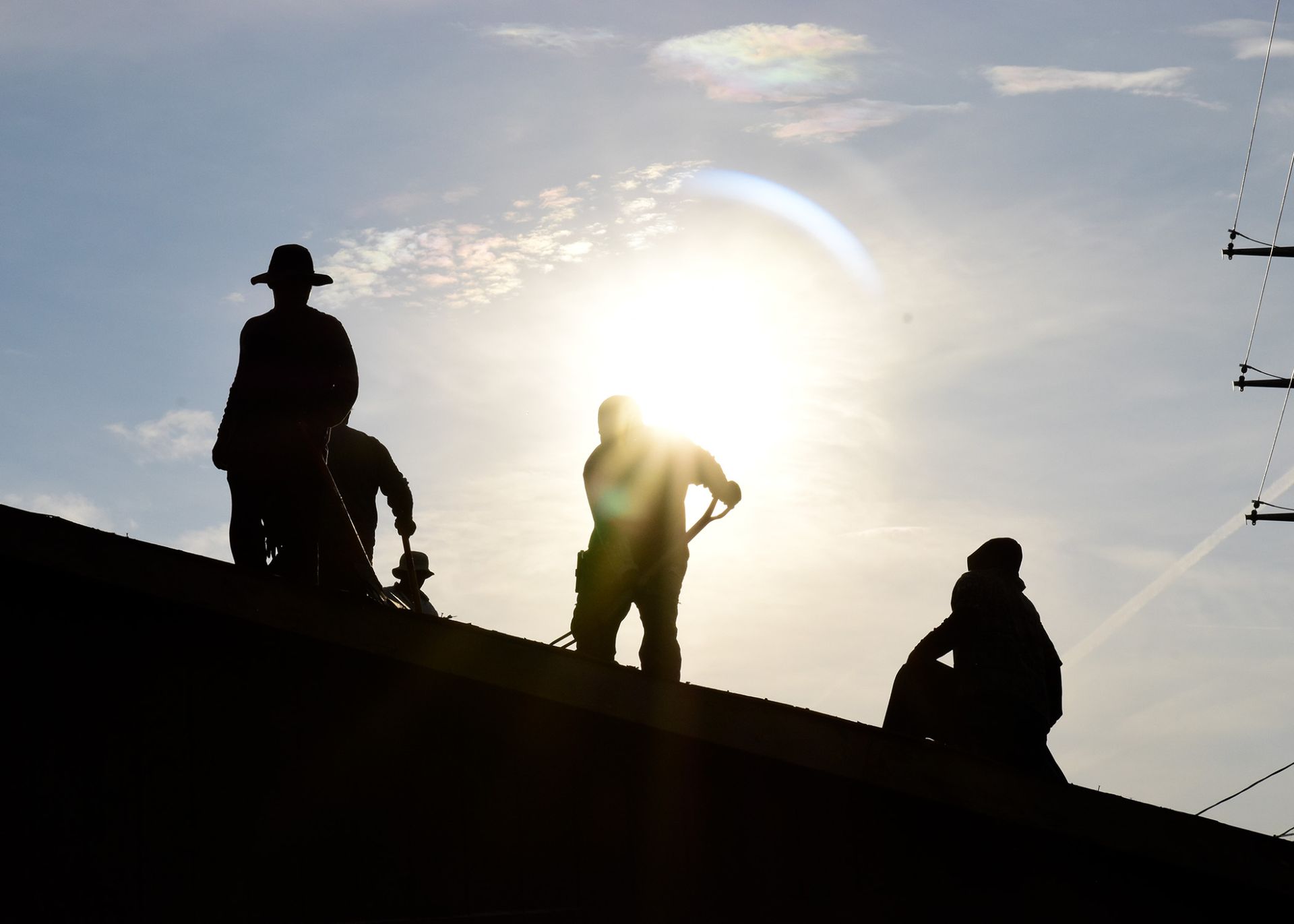 Silhouetted workers on a roof in bright sunlight.