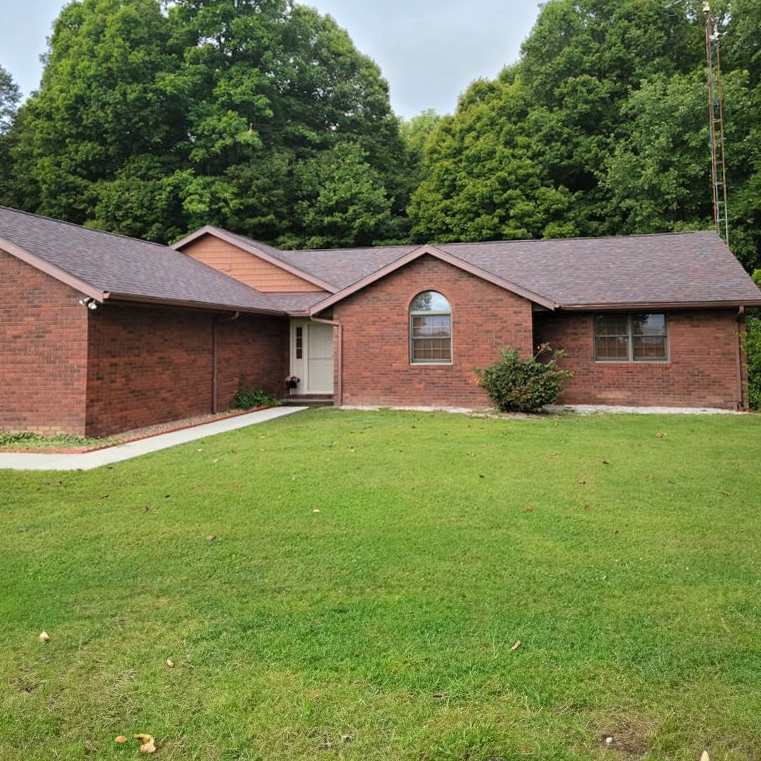 Red brick ranch-style house with green lawn, trees in background.