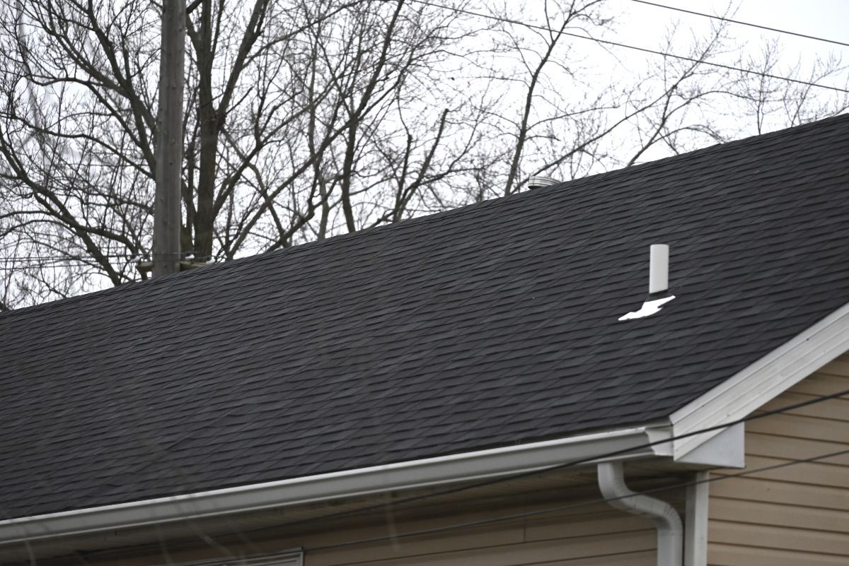 Black asphalt shingle roof with a white vent against a cloudy sky.