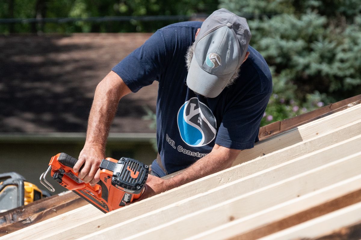 Person using a chainsaw on a wooden roof structure, outdoors.