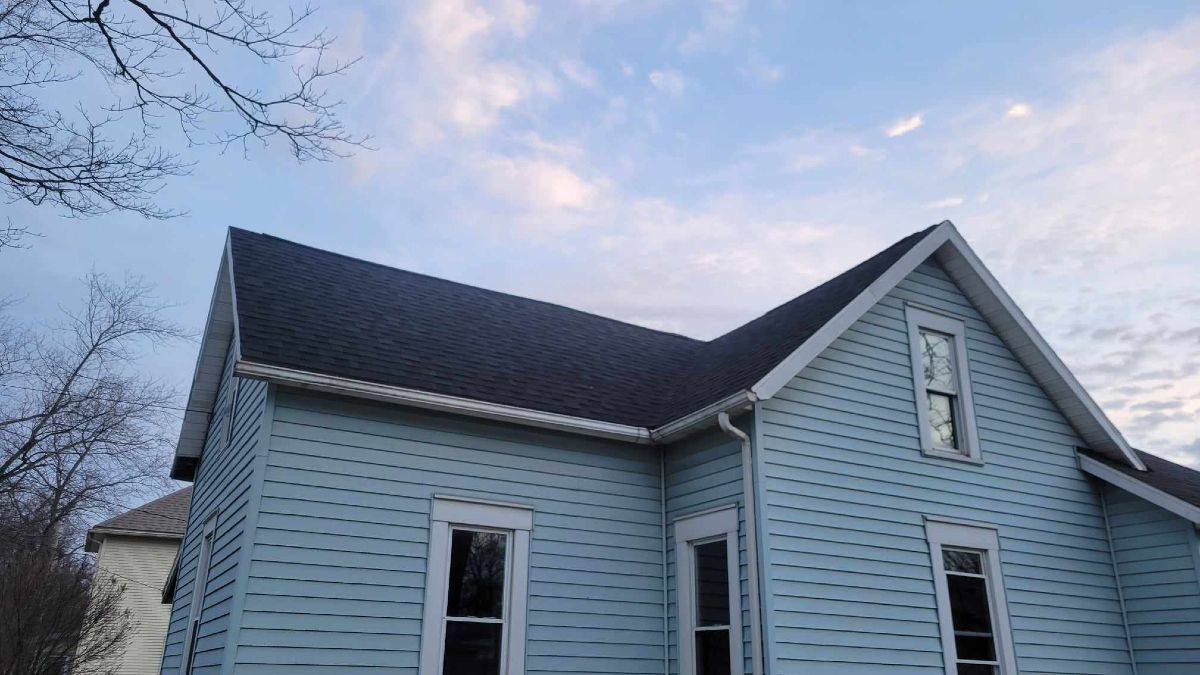 Blue house with dark roof against a cloudy sky.
