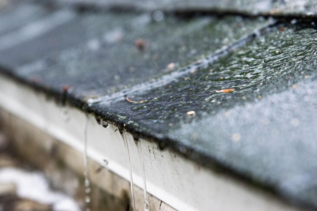 Close-up of a roof with water flowing off the edge into a gutter during a rainstorm.