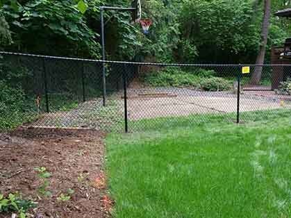 Backyard basketball court with chain-link fence and green lawn beside wooded area