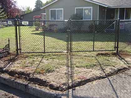 Chain-link gate in a front yard with a house and lawn behind it