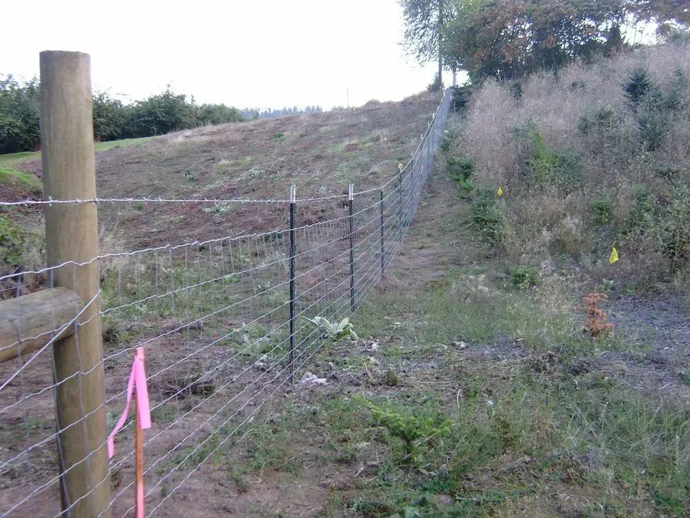 Wire fence along a grassy hillside with wooden posts and pink marker tape