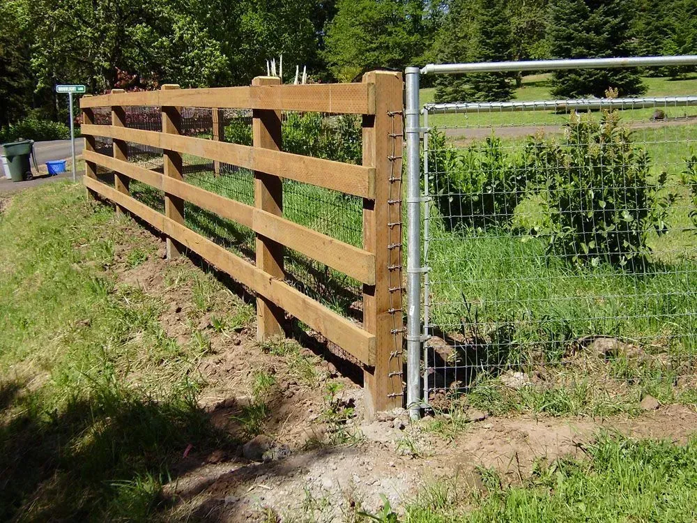 Wooden farm fence with wire mesh gate beside a grassy path in a sunny yard