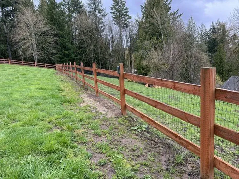 Wooden rail fence along a grassy field beside a wooded tree line under a cloudy sky