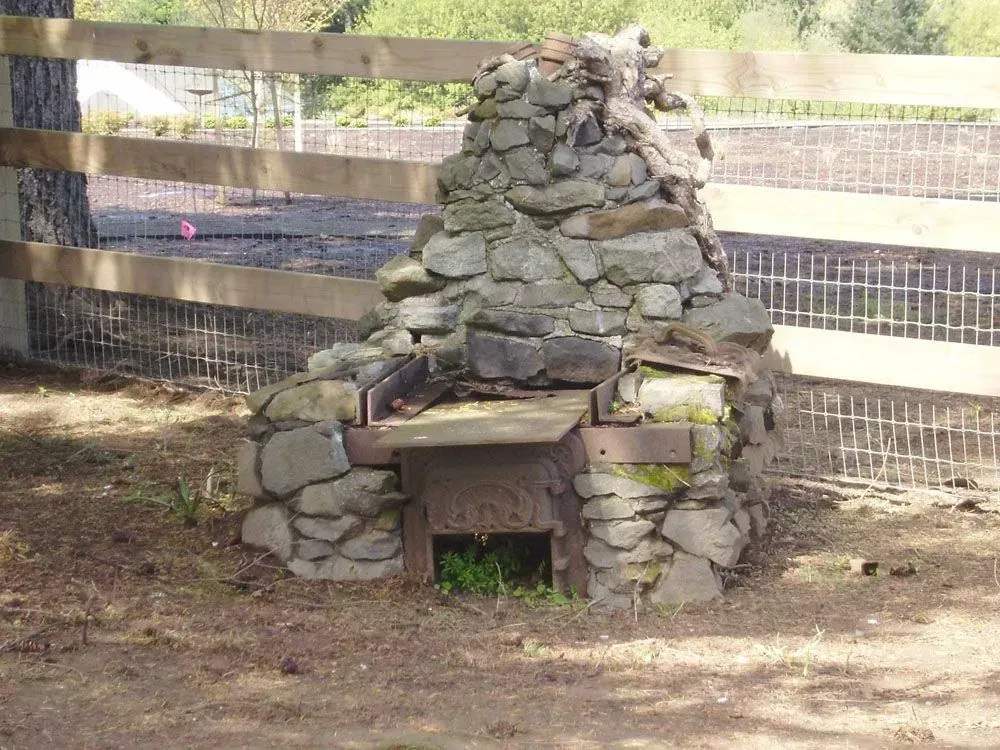 Stone outdoor fireplace or oven with wooden fence in a dirt yard