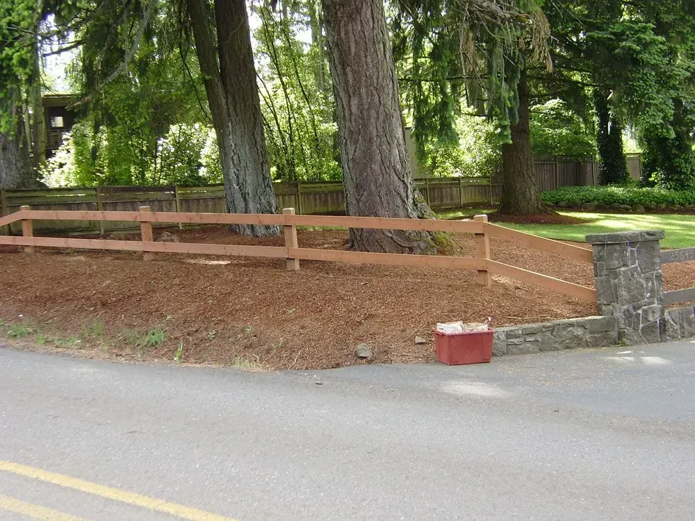 Wooden fence and stone gate beside a tree-lined road in a wooded park area
