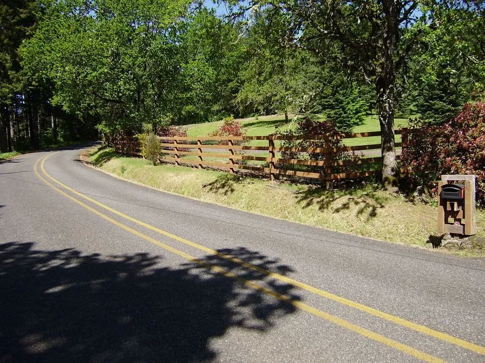 Curving country road with double yellow lines beside a wooden fence and trees in bright sunlight