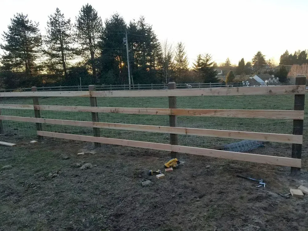 Wooden fence in a grassy field at sunset with trees and houses in the background