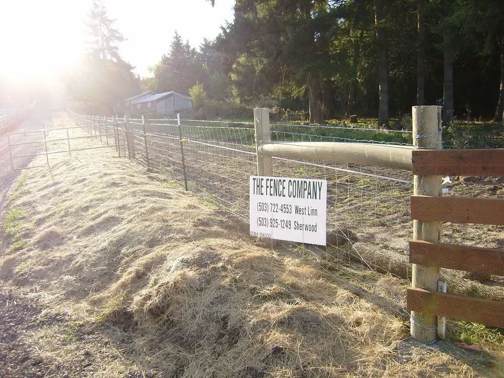 Sunny farm sign beside a fenced pasture with hay bales and trees