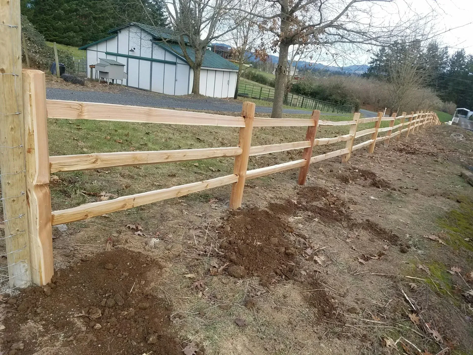 Wooden fence lining a dirt path beside a house on a hillside
