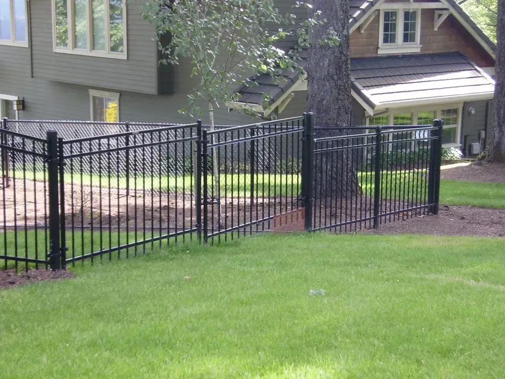 Black metal fence around a grassy yard in front of a house with trees and a driveway