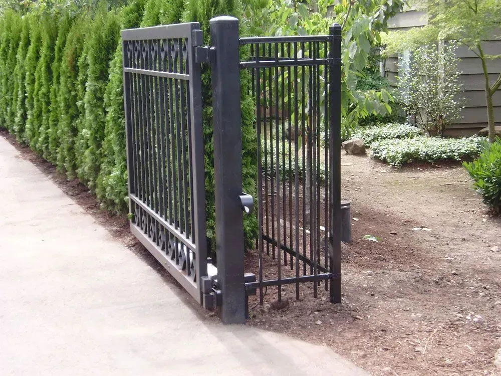 Black metal side gate beside a sidewalk and hedge in a garden area