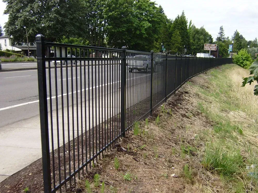 Black metal fence beside a roadside, with trees and grass along the embankment