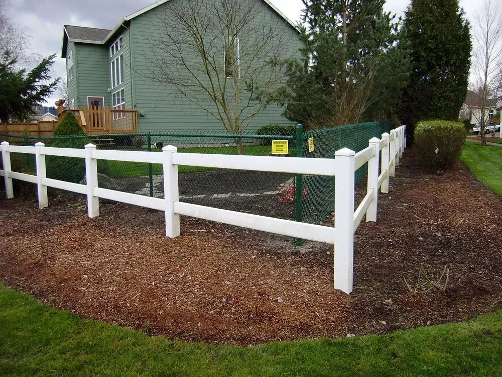 White fence around a green house and yard with mulch and a gravel path