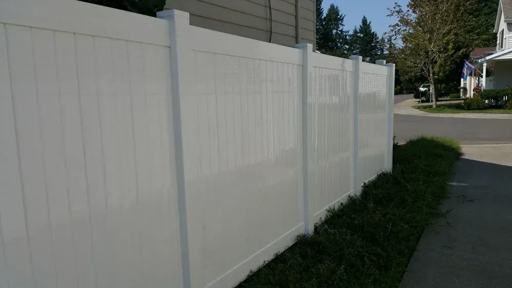White vinyl privacy fence along a suburban sidewalk beside a house and street.