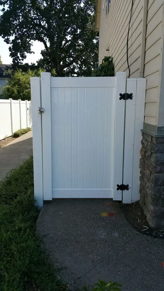 White wooden side gate beside a beige house, opening onto a paved driveway.