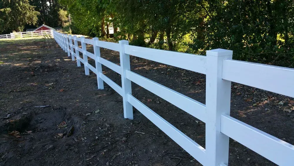 White wooden fence along a dirt path beside trees in a wooded area