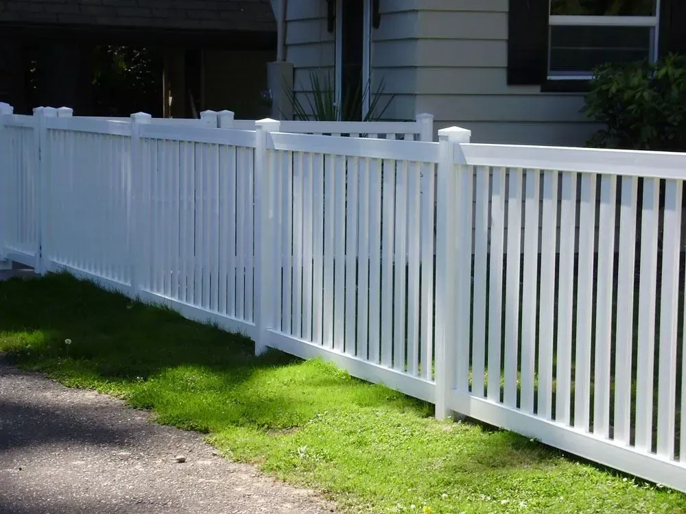 White picket fence along a grassy yard beside a house and driveway