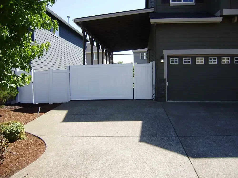 Driveway leading to a white gate beside a garage and house exterior.