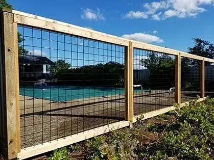 Wooden fence beside a blue pool and reflective glass building under a partly cloudy sky