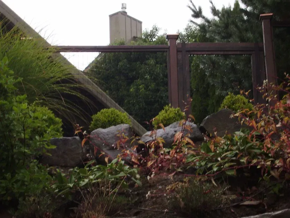 Rocky garden path with lush greenery and a metal railing near a building wall